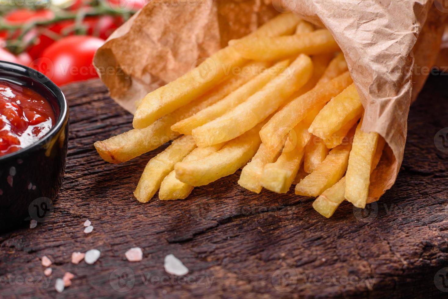 Batatas fritas saborosas frescas e molho vermelho em uma tábua de madeira foto