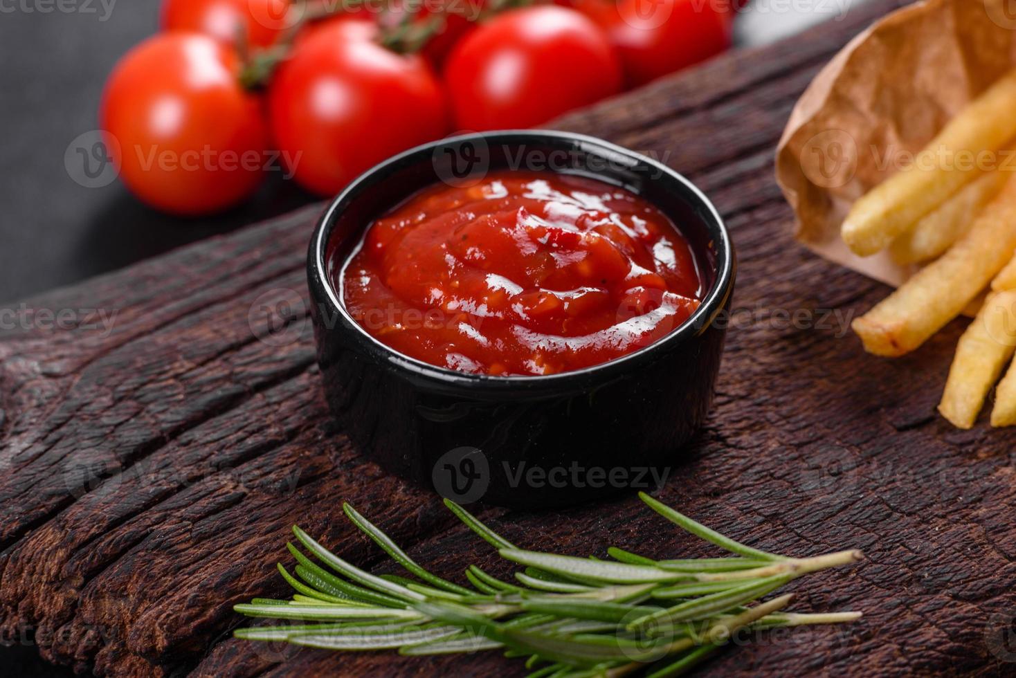 Batatas fritas saborosas frescas e molho vermelho em uma tábua de madeira foto