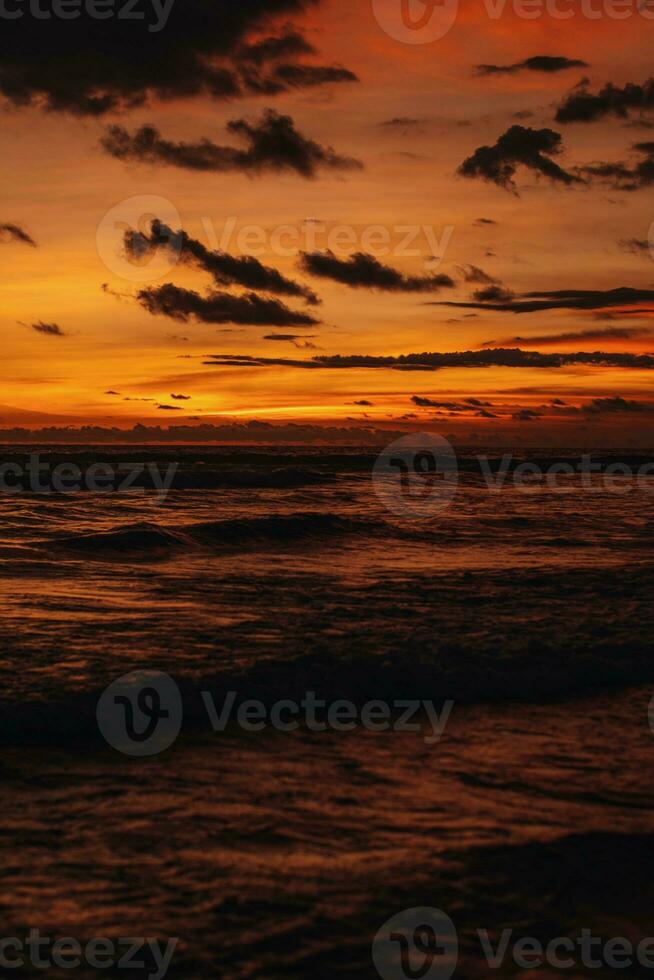 surpreendente brilhante laranja pôr do sol em a indiano oceano com ondas em bali ilha. tarde luz solar, fogo céu foto