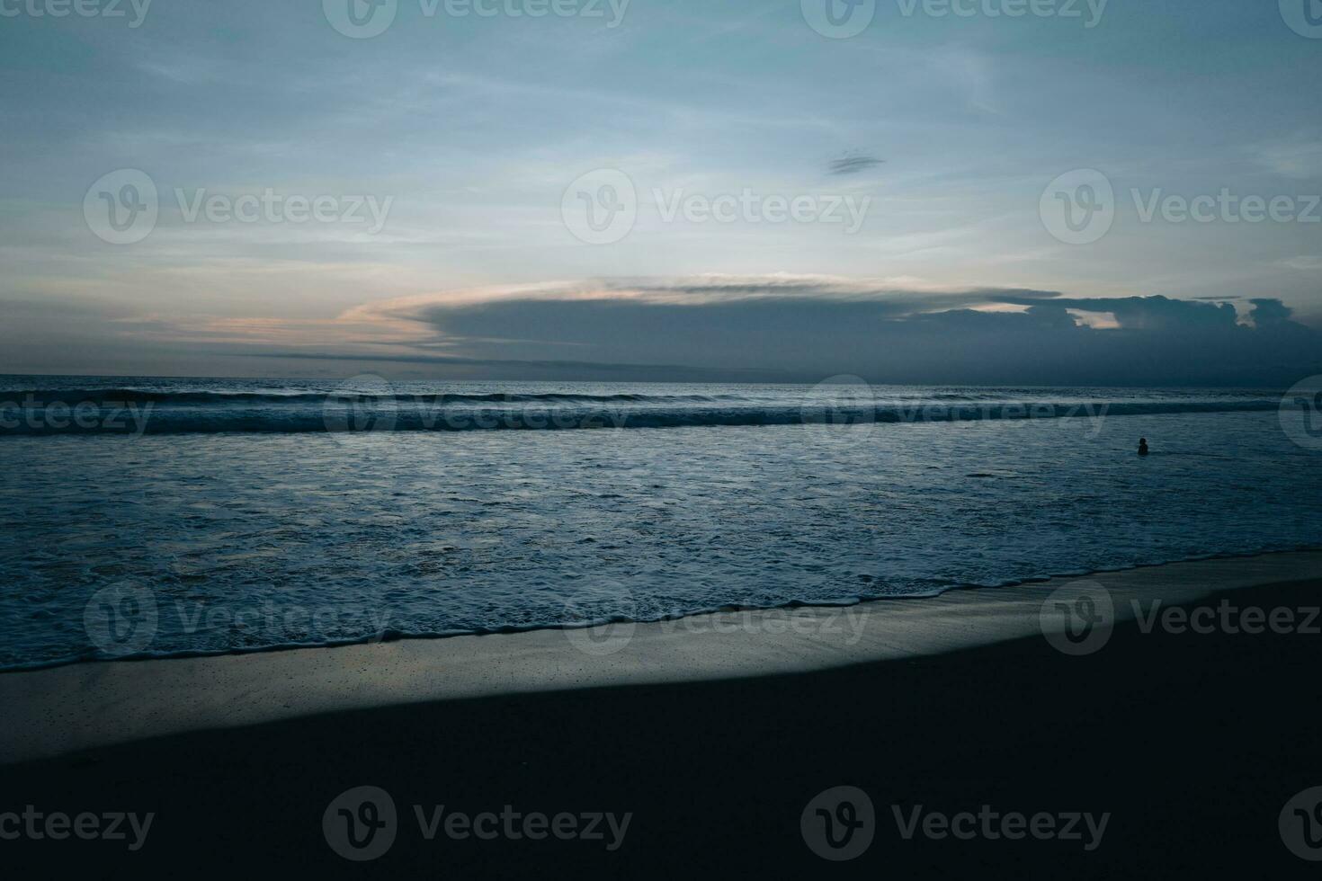 surpreendente tarde pôr do sol Sombrio azul céu em a indiano oceano com ondas em bali ilha. tropical verão fundo foto