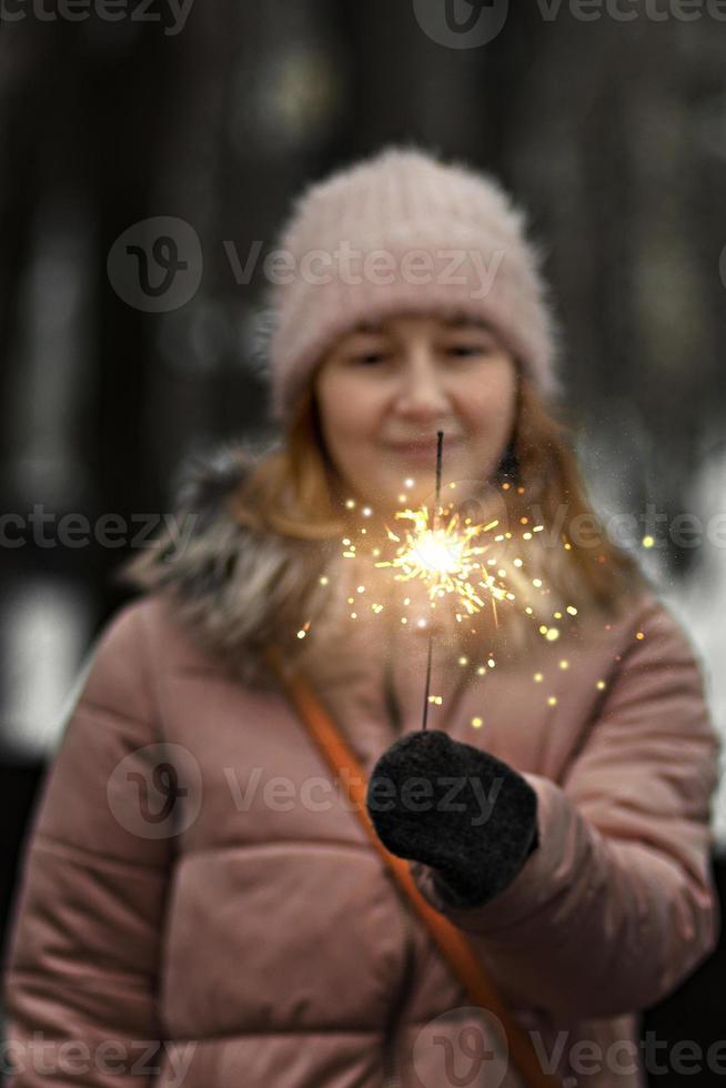 luzes de natal queimando nas mãos de uma mulher feliz embaçada no parque foto