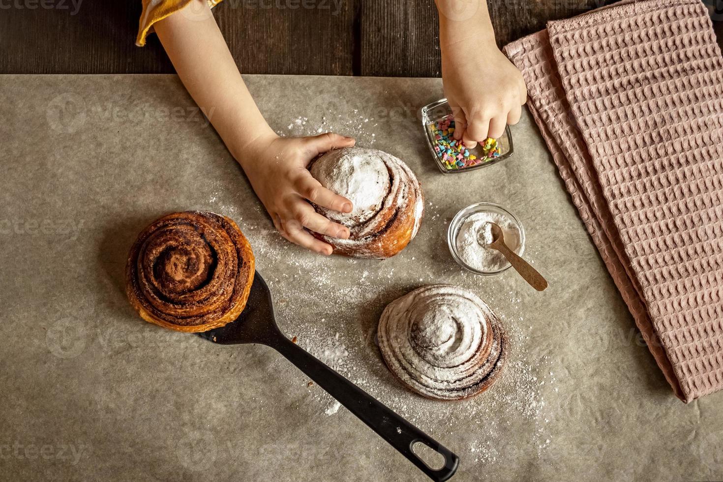 as mãos das crianças na moldura colocando granulado em um pão fresco assado foto