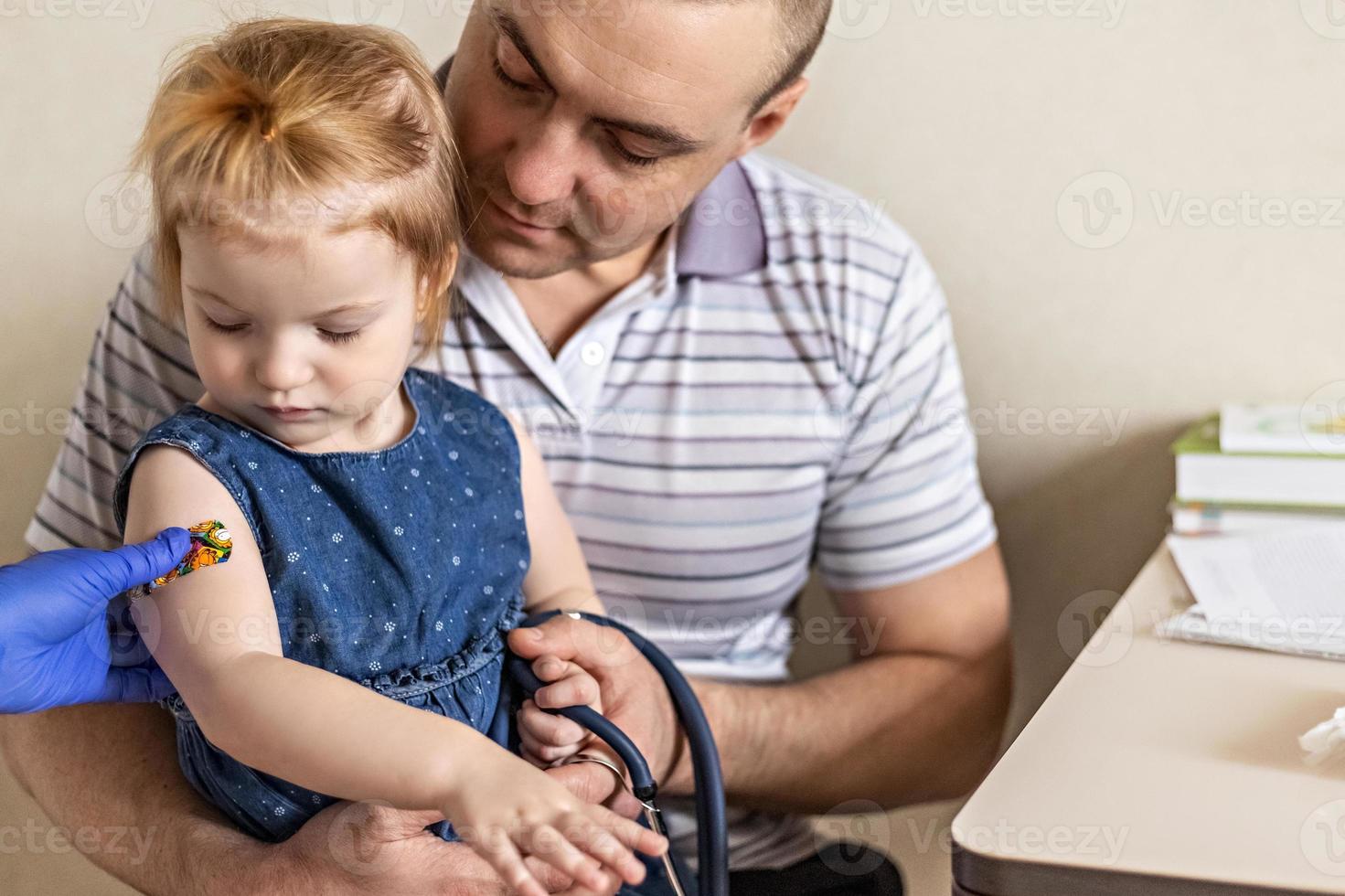 vacinação de uma menina nos braços do pai no consultório médico contra o coronavírus foto