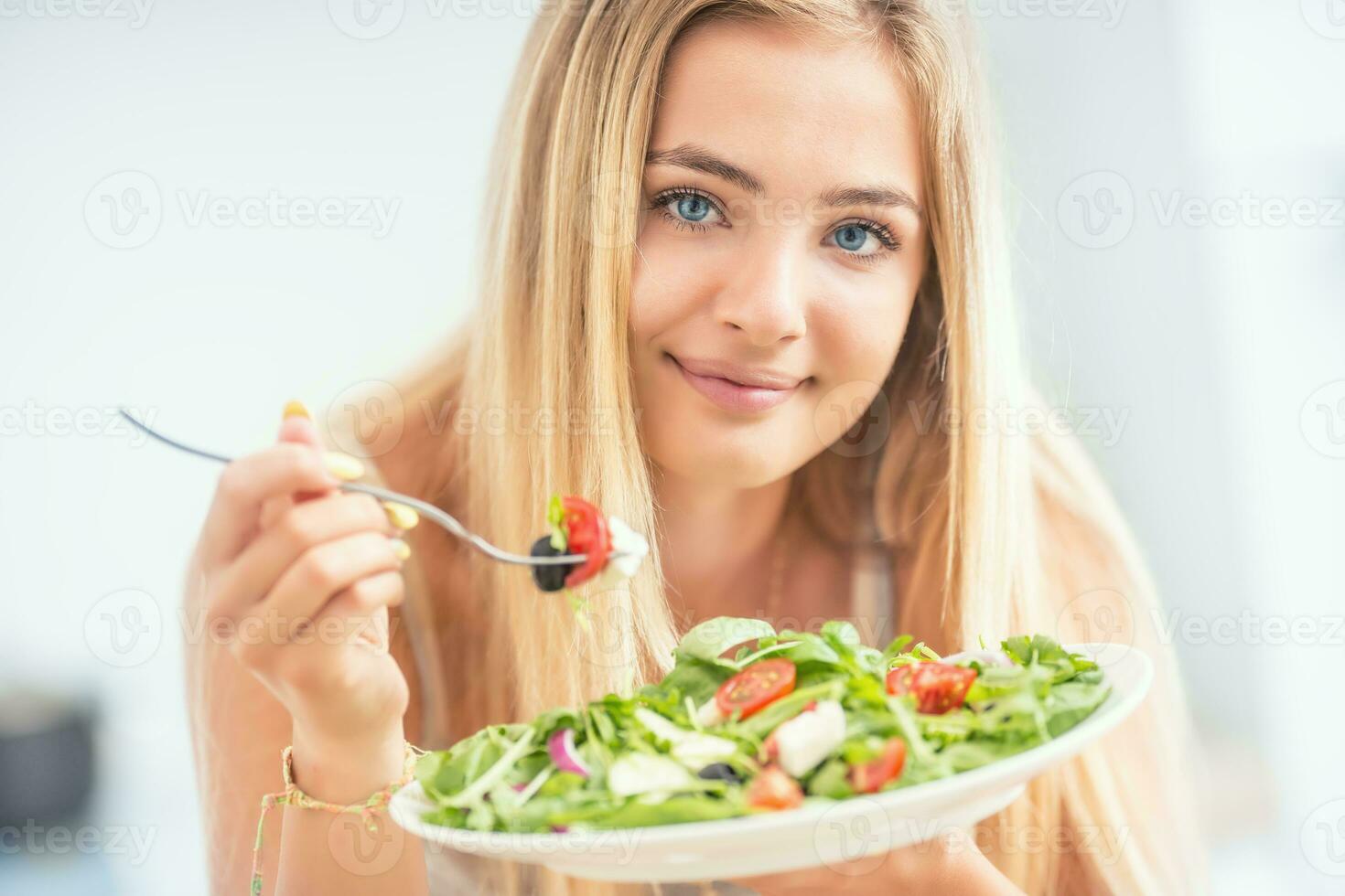 jovem feliz Loiras menina comendo saudável salada a partir de Rúcula espinafre tomates azeitonas cebola e Oliva óleo foto