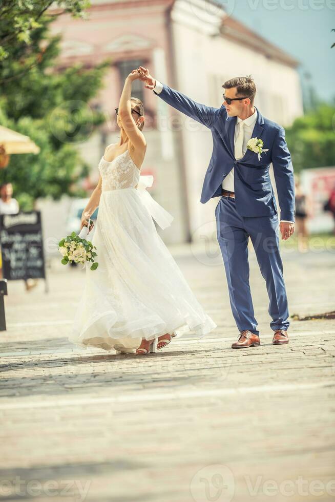 uma noivo dançando com dela noiva dentro a Cidade depois de uma casamento. ainda vestindo lindo vestes e segurando uma ramalhete fez do branco flores foto