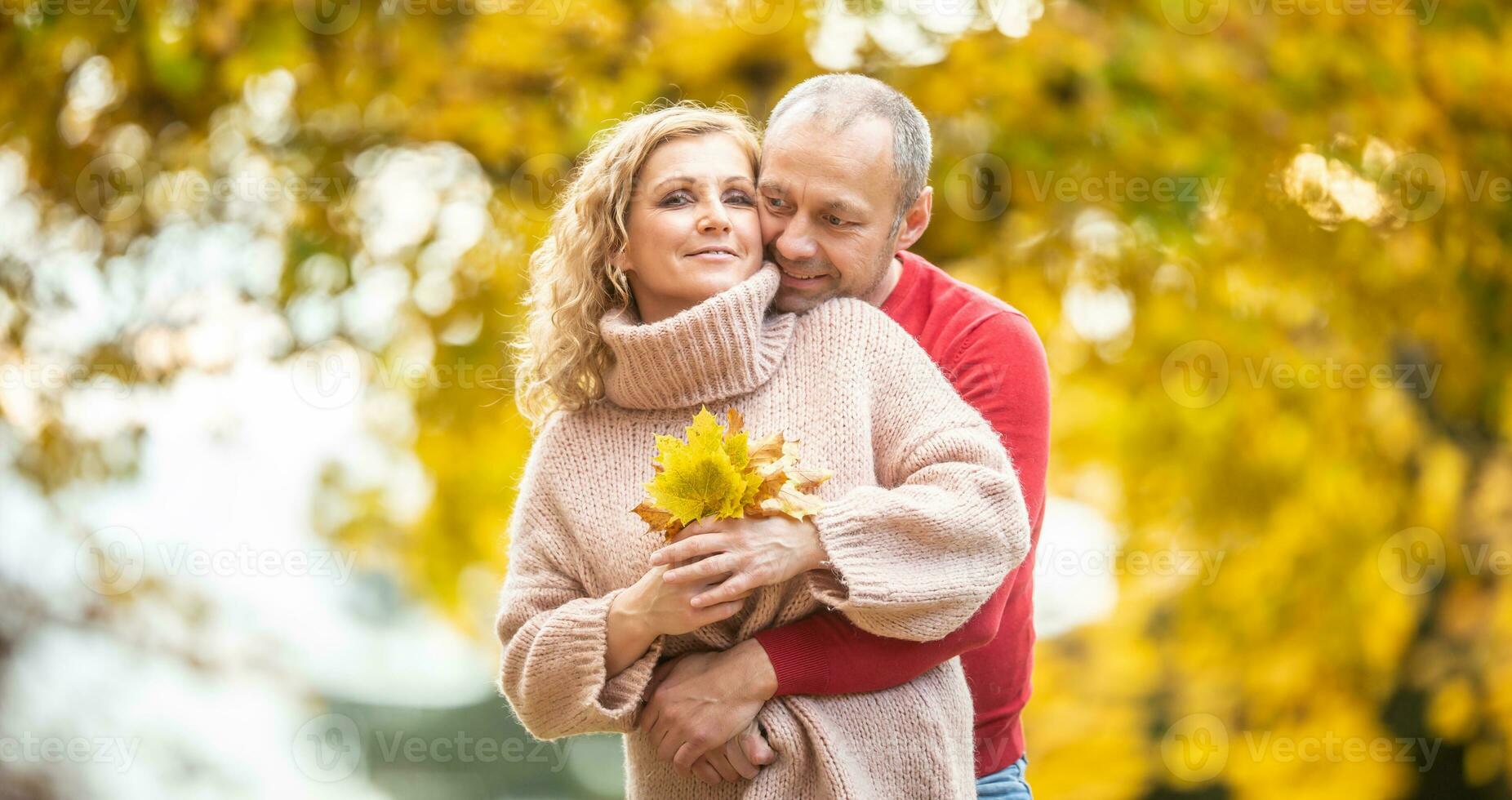 casal ações seus amor abraçando, segurando caído outono folhas cercado de amarelo árvores foto