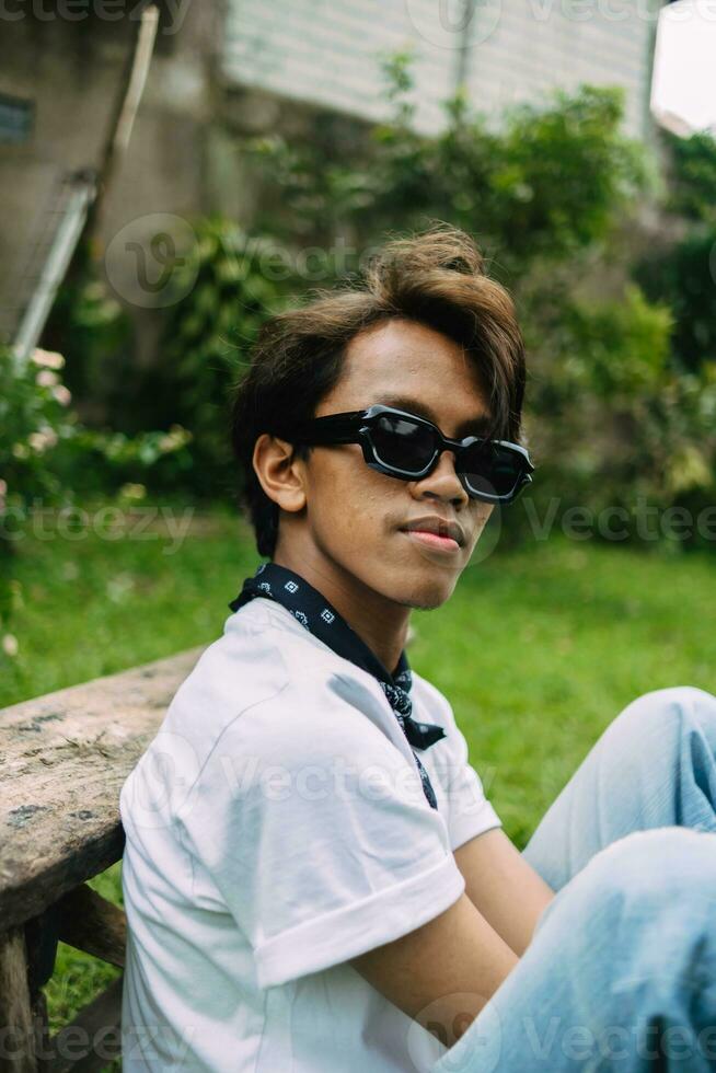 a ásia adolescente com oculos de sol e Loiras cabelo é relaxante dentro a quintal jardim foto