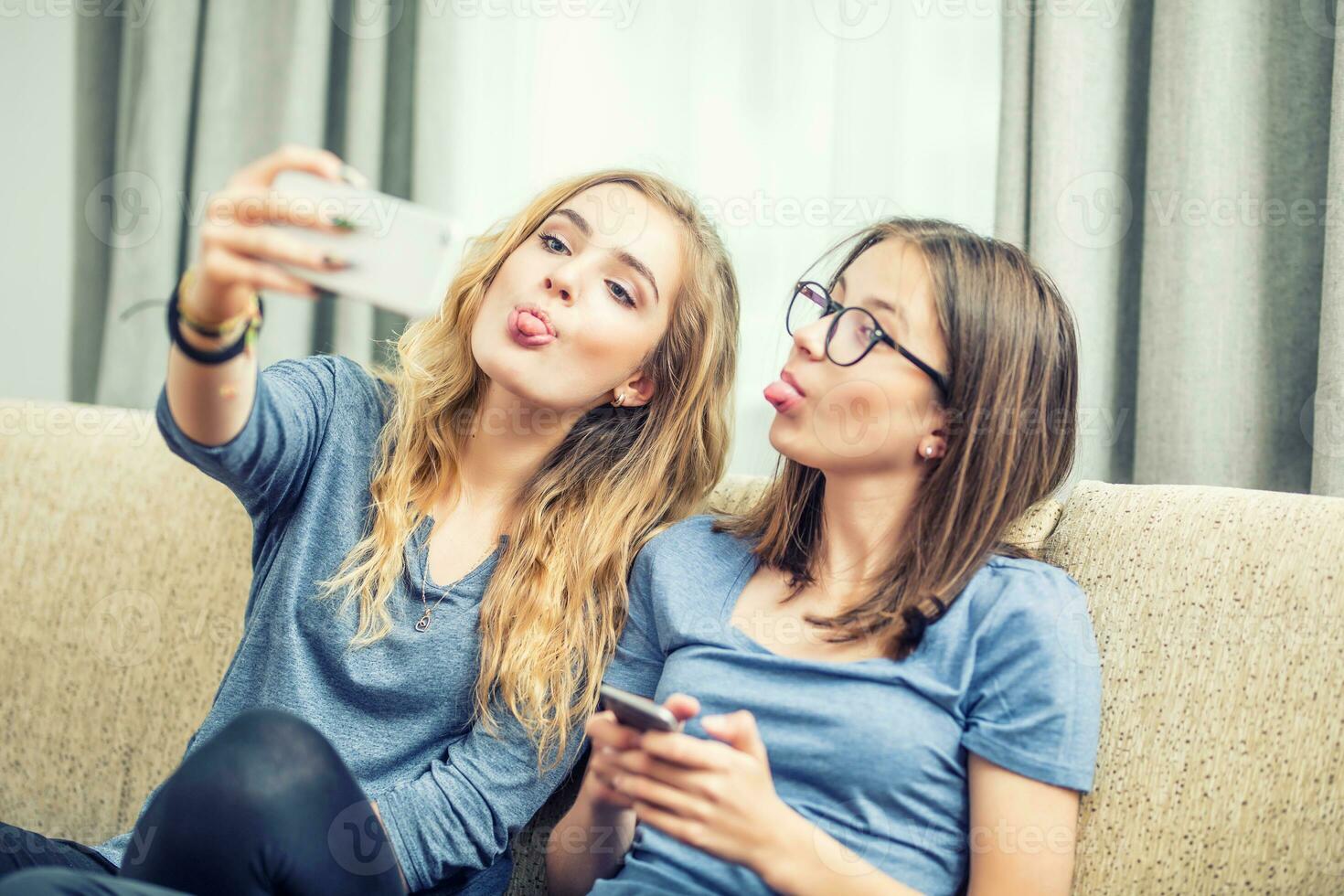 dois adolescente meninas sorrir e levar uma selfie junto. elas faço caretas Fora do seus língua foto