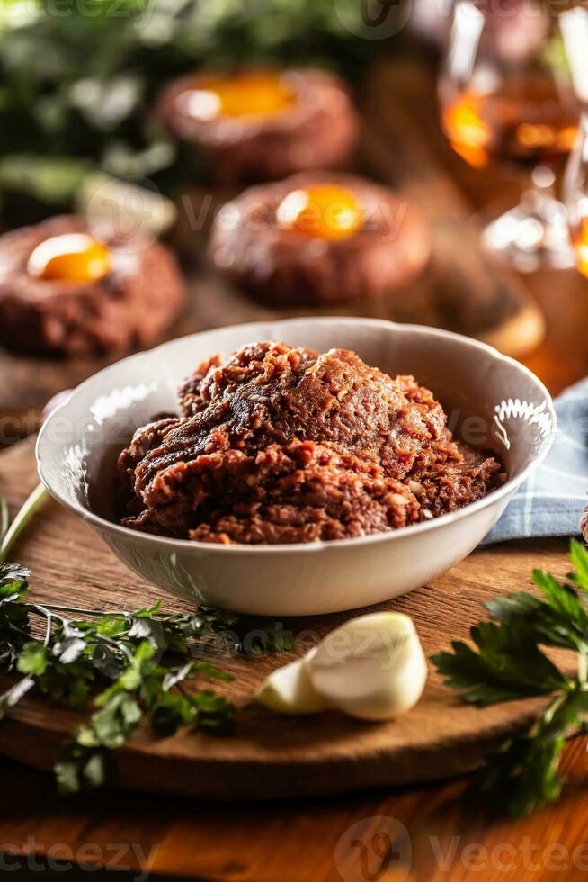 branco tigela preenchidas com cru carne pronto para preparar delicioso bife tartare com salgado ovo gemas. já preparado tártaros dentro a Backgroud com rum e ervas Como uma decoração foto