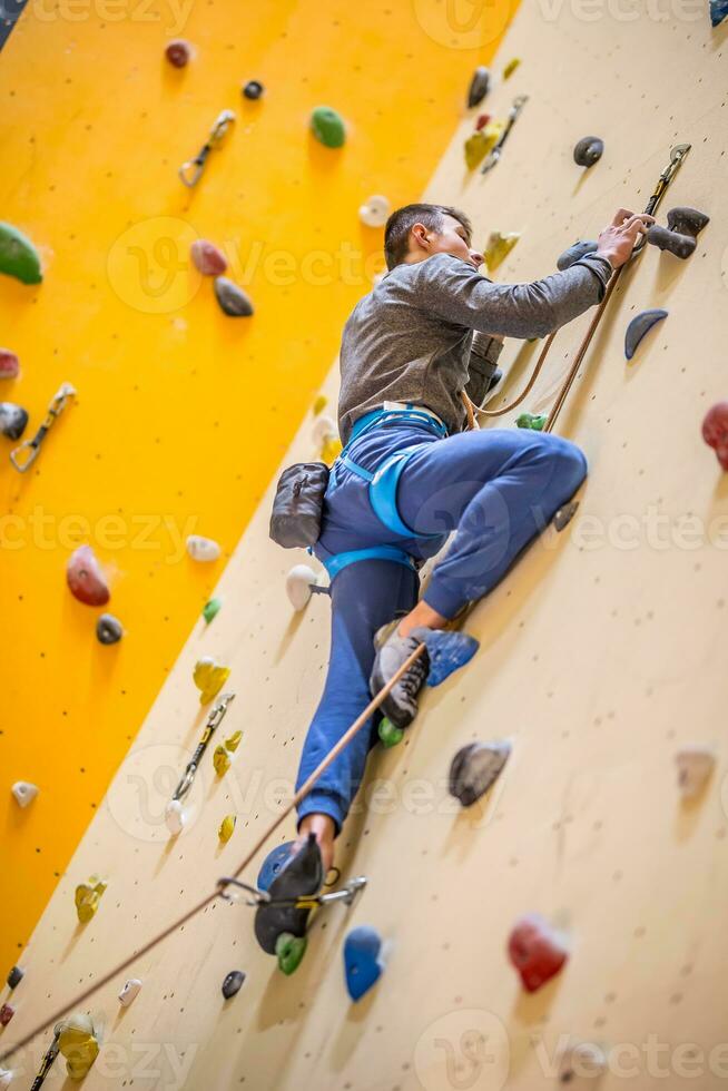 alpinista em parede.jovem homem praticando Rocha escalada em uma Rocha parede dentro de casa foto