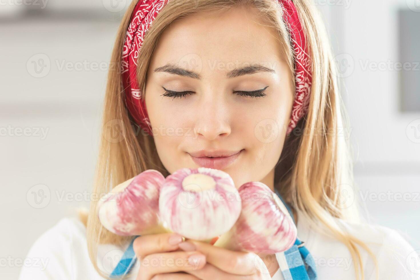 uma jovem dona de casa é segurando fresco alho e cheirando isto foto