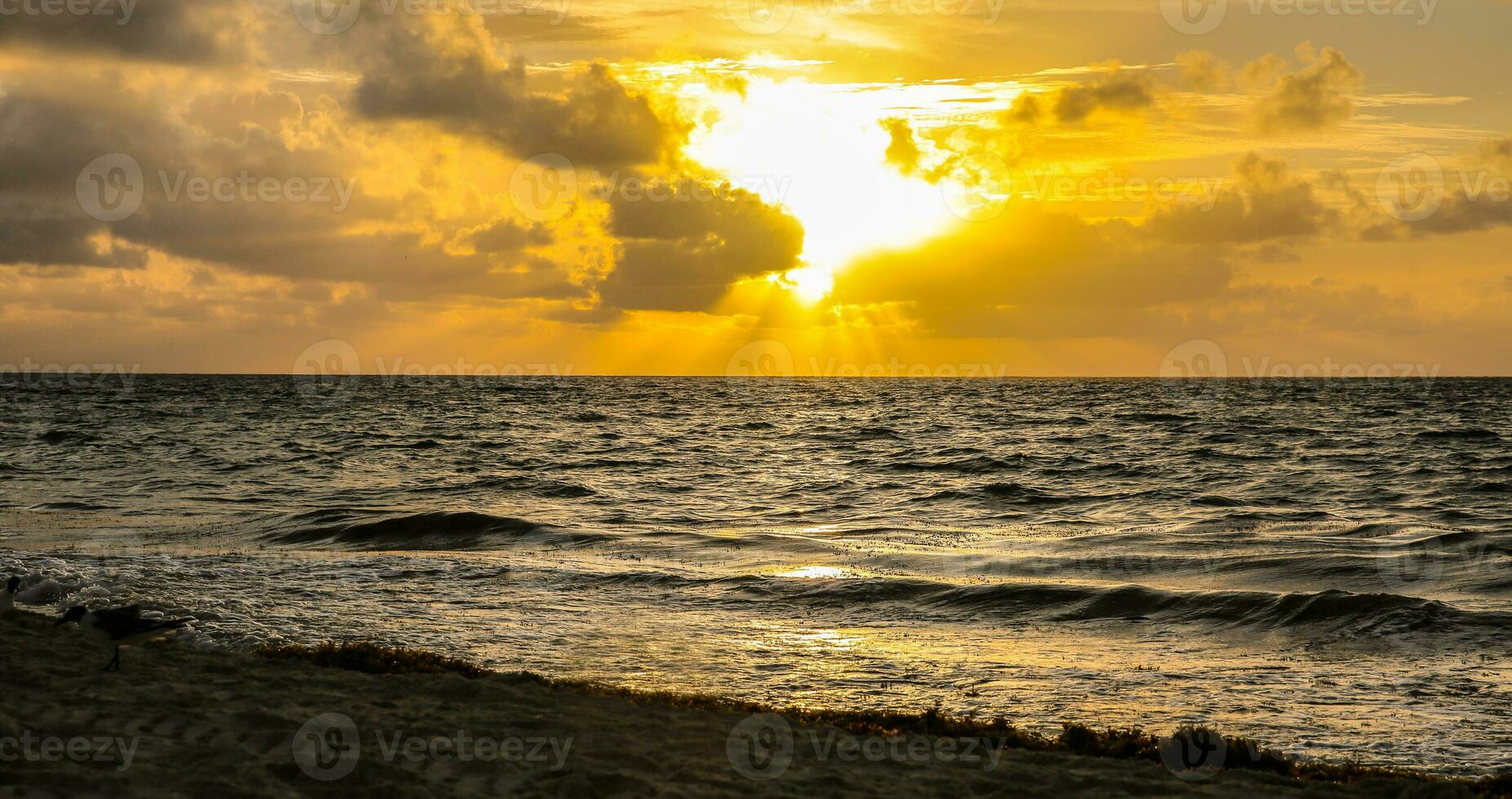 nascer do sol ou uma pôr do sol acima a mar ocupado a partir de uma arenoso praia, parcialmente escondido de a nuvens foto