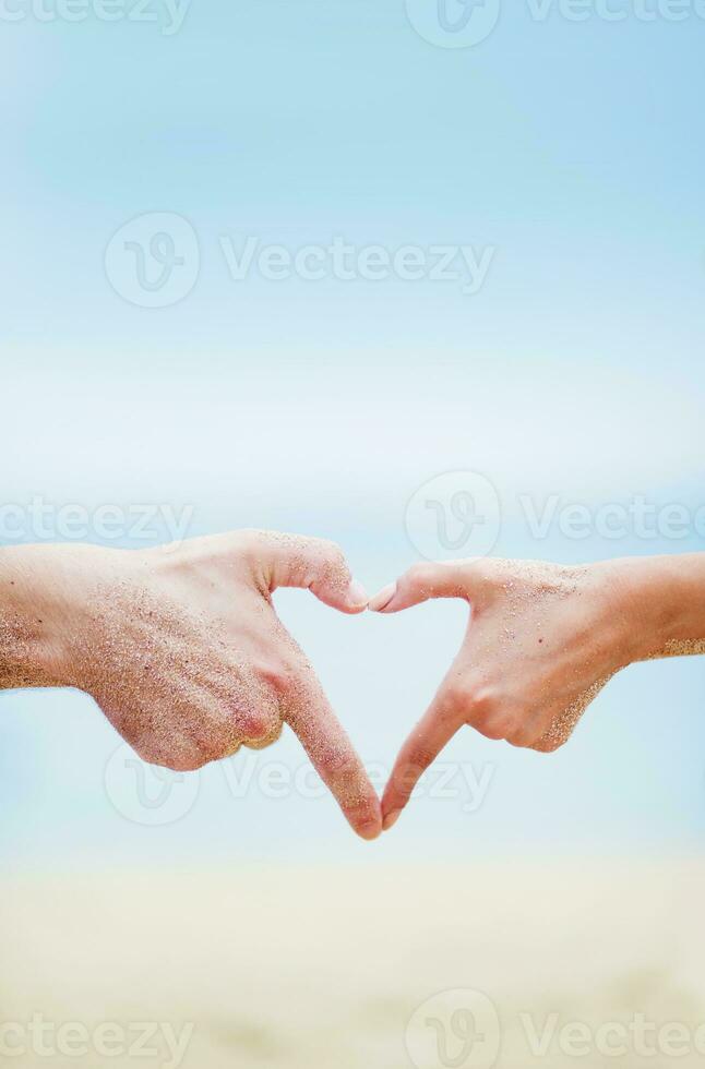 dois pessoas fazer uma coração forma com seus mãos em a de praia foto