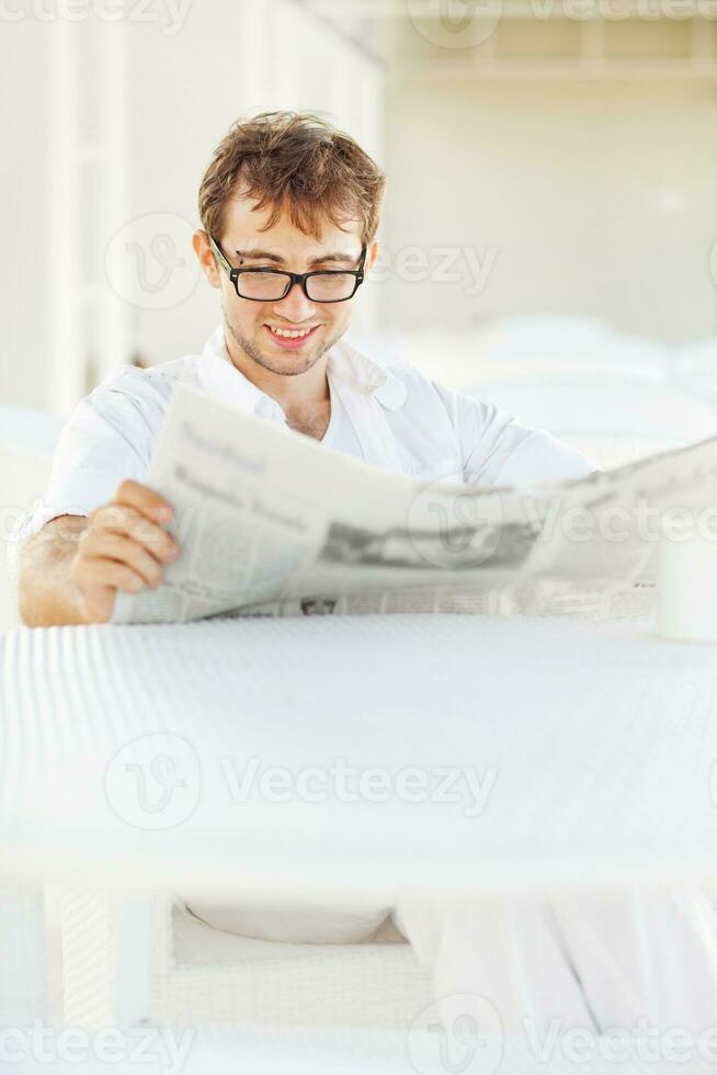 uma homem dentro óculos lendo uma jornal enquanto sentado às uma mesa foto