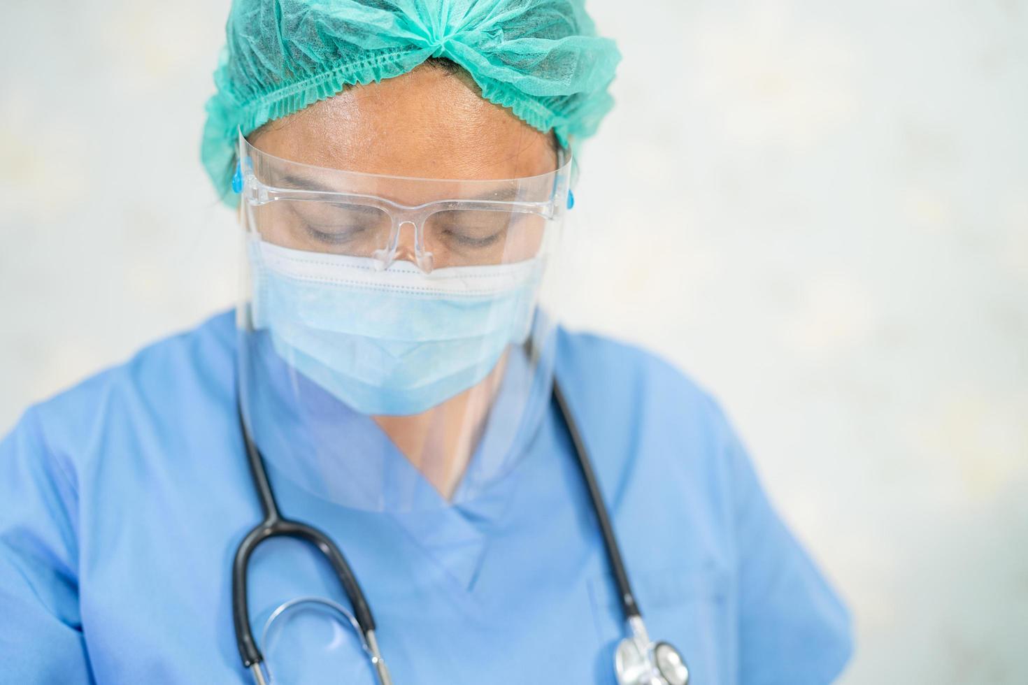 médico asiático usando protetor facial e terno novo normal para verificar o paciente protege a segurança infecção covid-19 surto de coronavírus na enfermaria de quarentena do hospital. foto