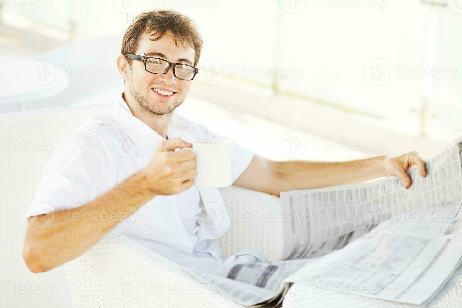 uma homem dentro óculos lendo uma jornal enquanto sentado às uma mesa foto