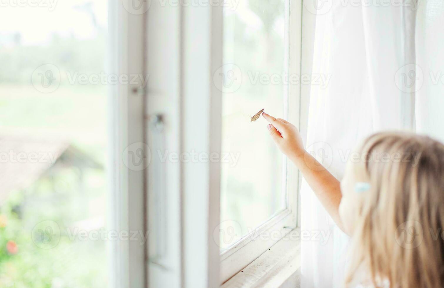 uma pequeno menina tocante uma borboleta em a janela foto