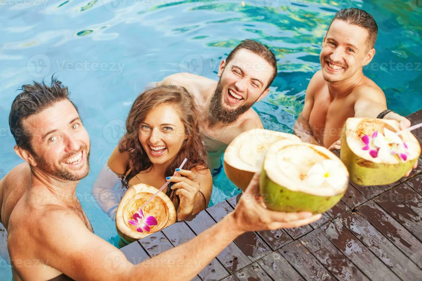 quatro amigos segurando coco bebidas dentro a piscina foto