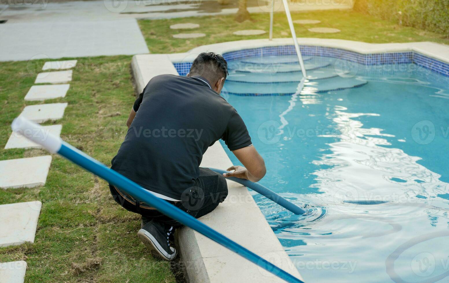 manutenção pessoa limpeza natação piscina com sucção mangueira. limpeza e manutenção do natação piscinas com sucção mangueira. agachado homem limpeza natação piscina com vácuo mangueira foto