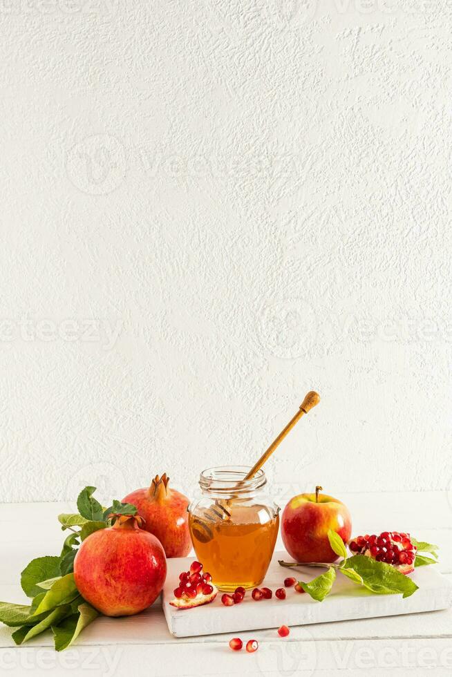 lindo ainda vida com maduro romãs e maçãs, uma tigela do mel. branco fundo. a conceito do rosh hashaná. uma cópia de espaço. vertical visualizar. foto