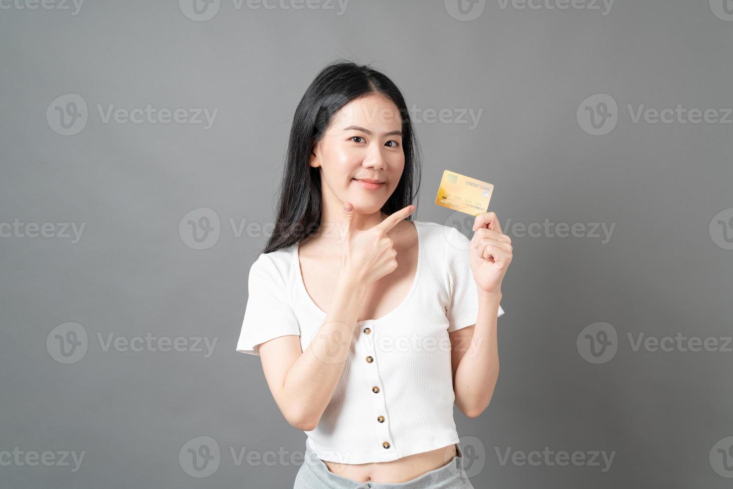 mulher asiática com cara feliz e apresentando cartão de crédito na mão, mostrando confiança e segurança para fazer o pagamento foto