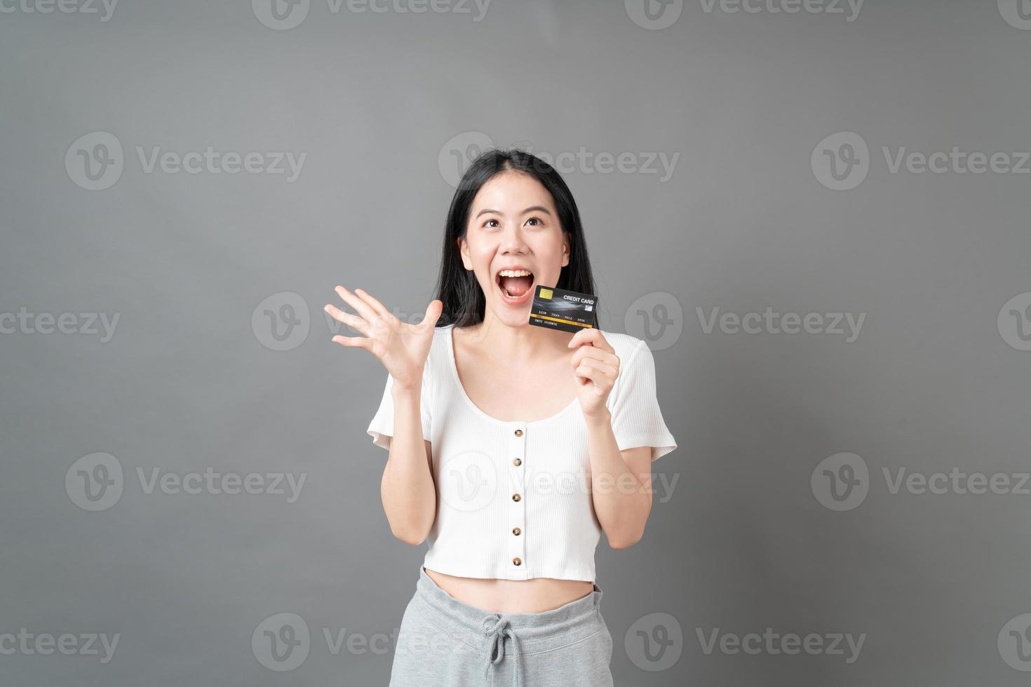 mulher asiática com cara feliz e apresentando cartão de crédito na mão, mostrando confiança e segurança para fazer o pagamento foto