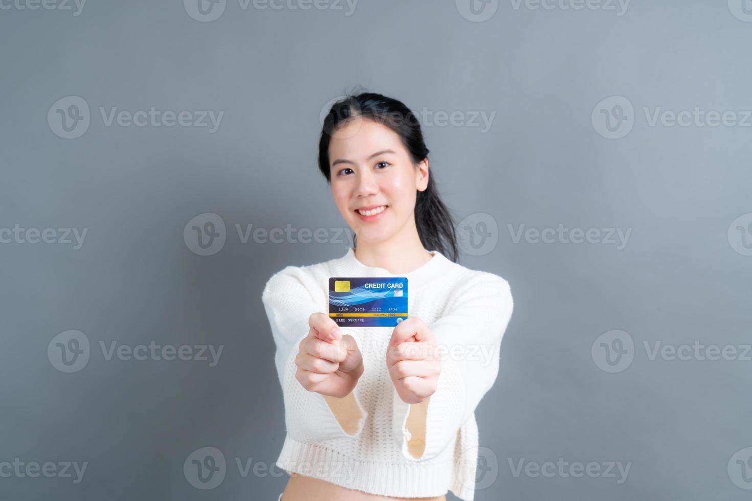 retrato de uma linda jovem asiática de suéter mostrando um cartão de crédito com espaço de cópia foto