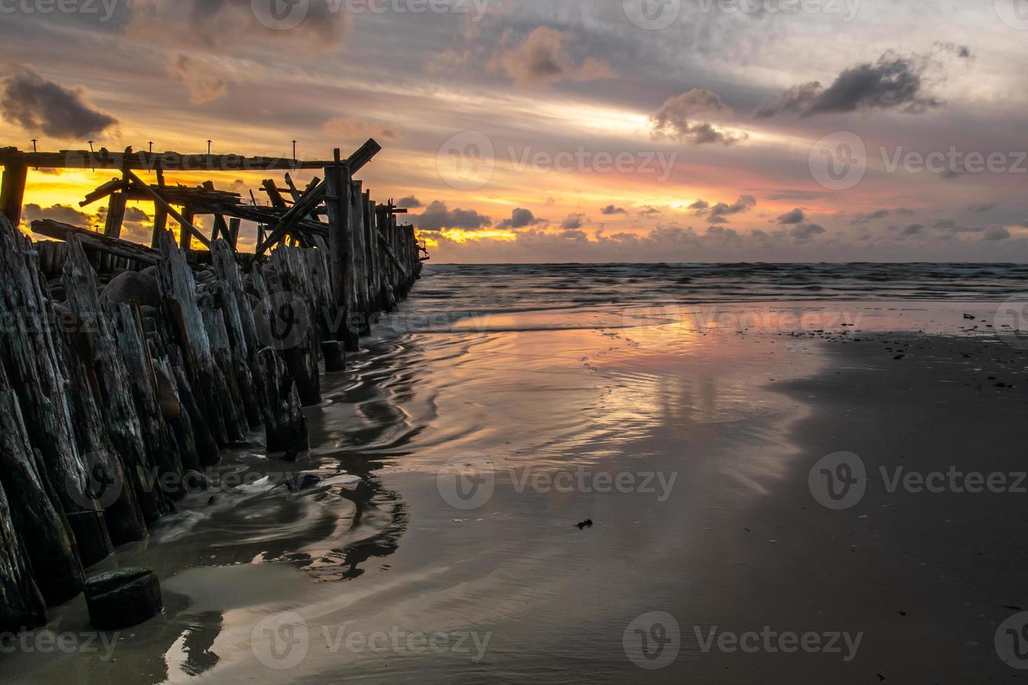 ruínas do quebra-mar de madeira e seu reflexo na superfície da areia molhada ao pôr do sol foto