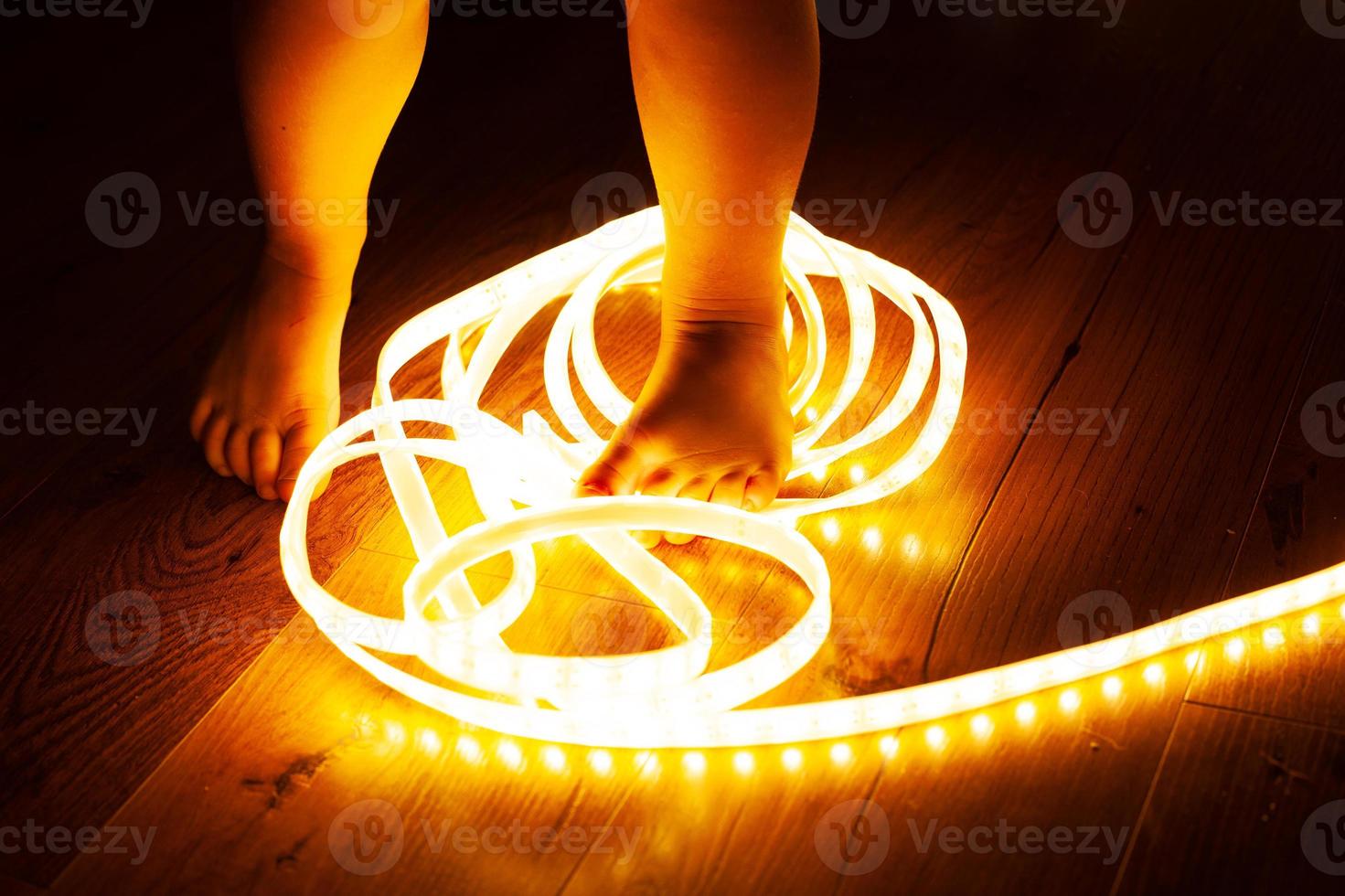 Pernas de bebê, menina pisando na faixa de led, bebê travesso brincando com eletricidade, conceito de segurança infantil e close-up do controle dos pais foto