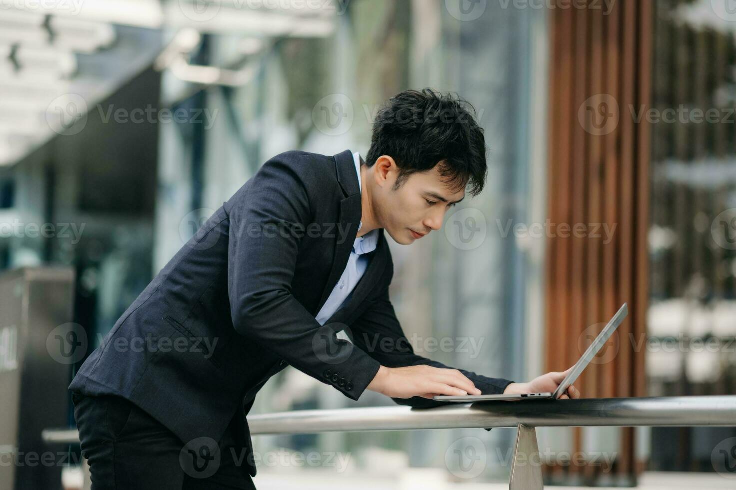 confiante ásia homem com uma sorrir em pé segurando bloco de anotações e tábua às a moderno escritório. foto