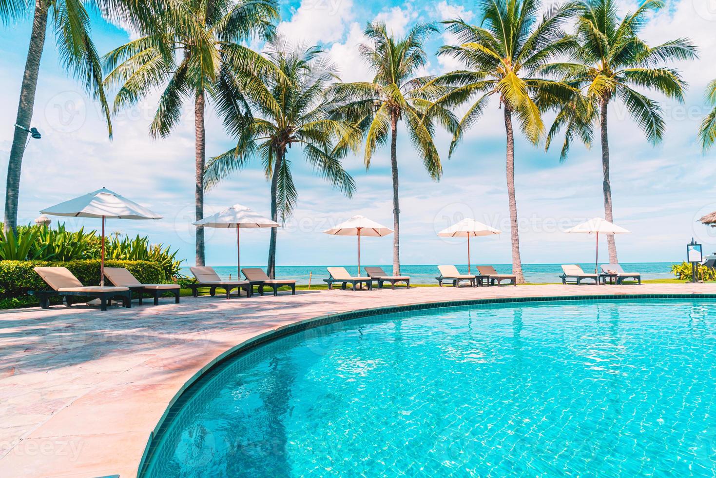 bela praia tropical e mar com guarda-sol e cadeira ao redor da piscina em hotel resort foto