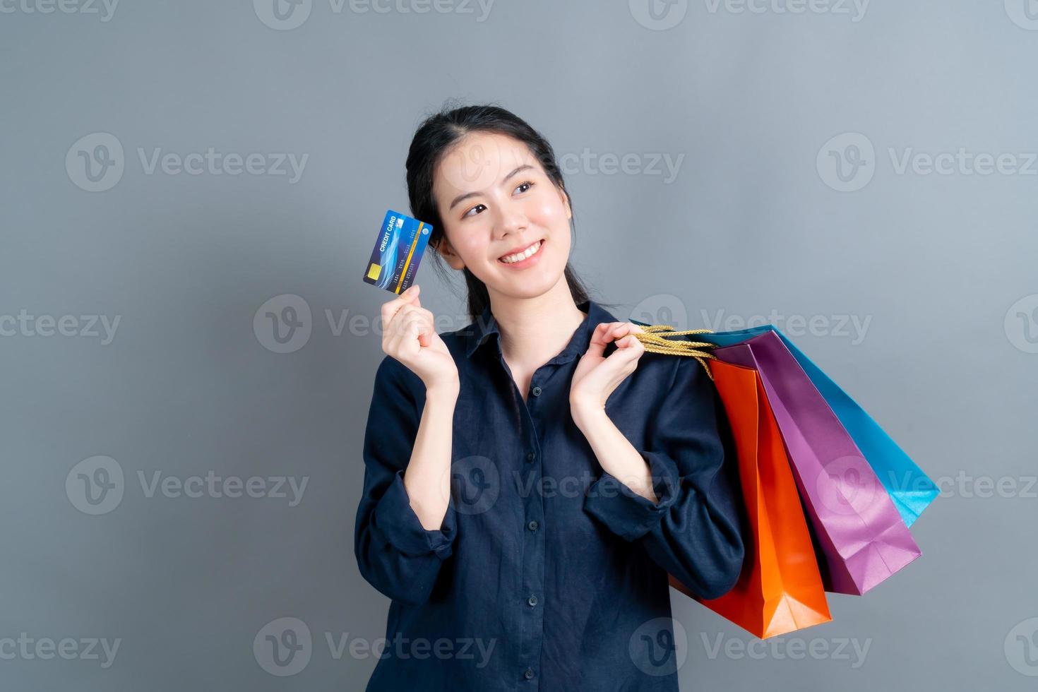 linda mulher asiática com sacolas de compras e apresentando cartão de crédito foto