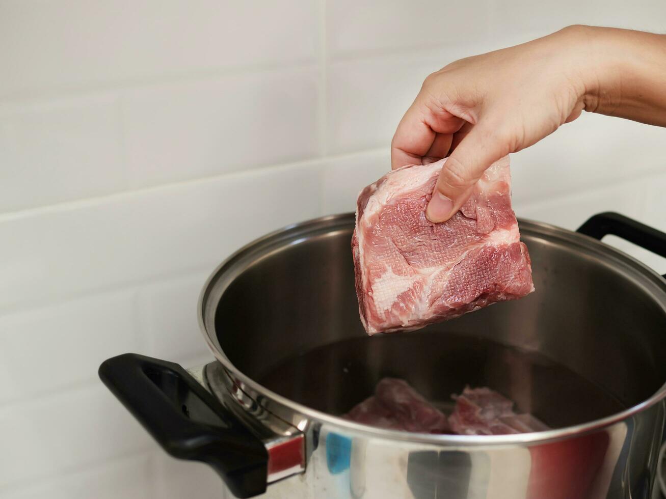 senhora colocando cru carne de porco Picar dentro metal Panela para preparando sopa dentro branco limpar \ limpo casa cozinha, casa cozinhando conceito foto