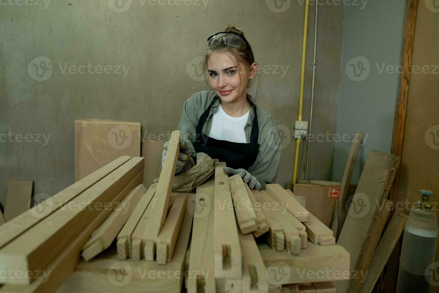 trabalha duro carpinteiro mulher usando Ferramentas sorridente com confiança jovem fêmea marceneiro dentro avental em pé perto bancada e olhando às Câmera amigáveis enquanto trabalhando dentro a construir oficina foto