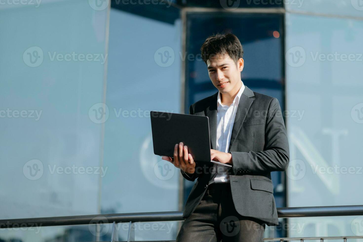 jovem ásia o negócio homem trabalhando às lado de fora o negócio Centro com computador portátil, tábua, Smartphone e levando notas em a papel. foto