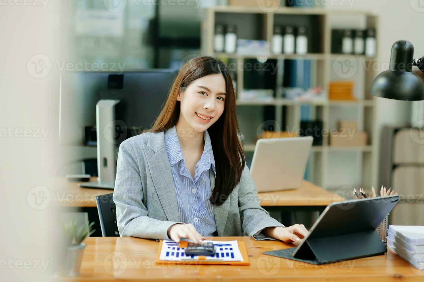 mulher asiática confiante com um sorriso em pé segurando o bloco de notas e tablet no escritório moderno. foto