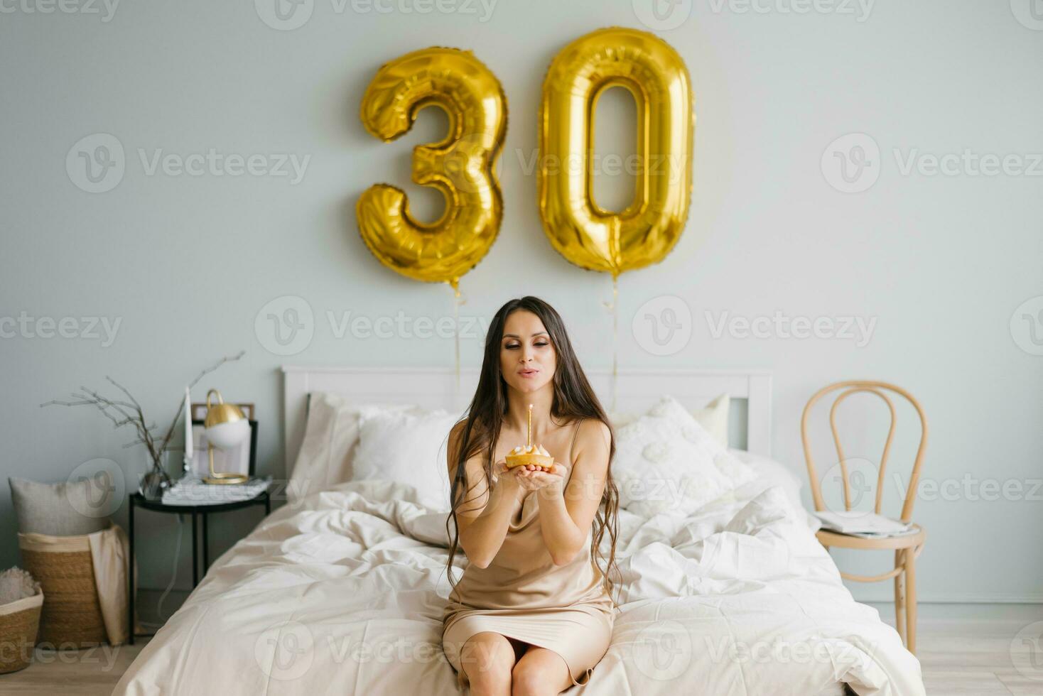 fofa caucasiano menina dentro uma camisola, quem é parabenizado em dela aniversário dentro cama, golpes Fora uma vela em uma bolo e faz uma desejo para uma celebração, estilo de vida e feriado conceito. foto