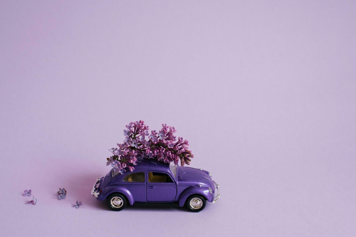 roxa brinquedo carro com lilás flores em a cobertura em uma lilás fundo. flor Entrega. aniversário feriado conceito, mãe dia, dia dos namorados dia, Primavera dia foto