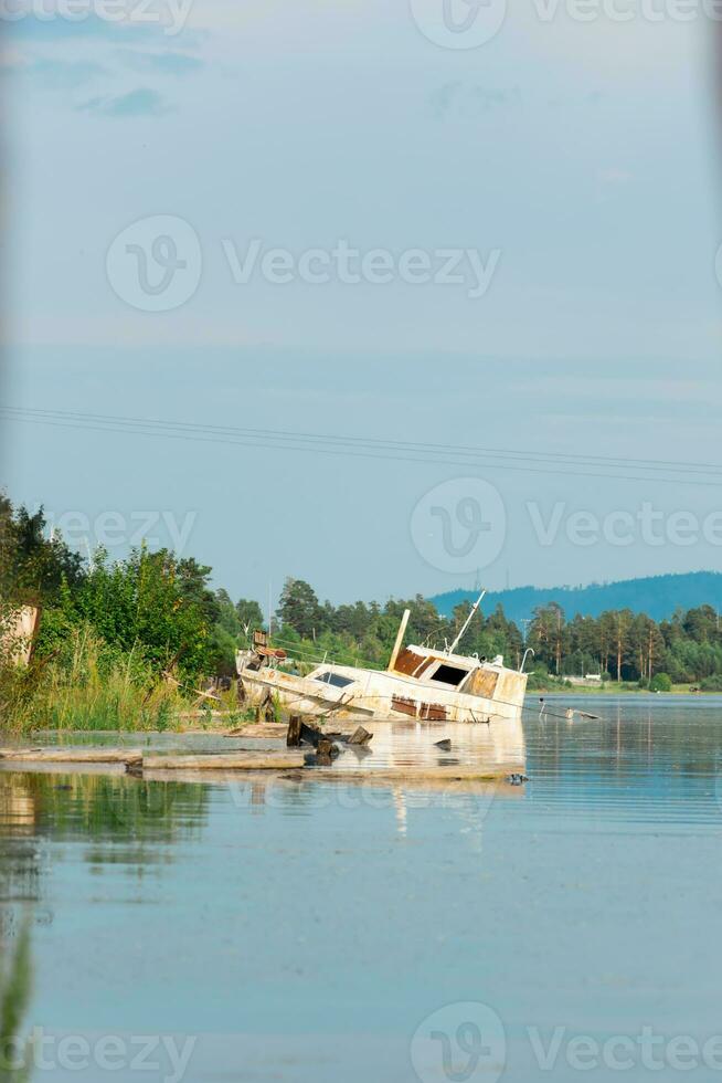 velho oxidado barco encalhado em a costa do a rio baía. humano poluição de industrial desperdício. vertical Visão foto