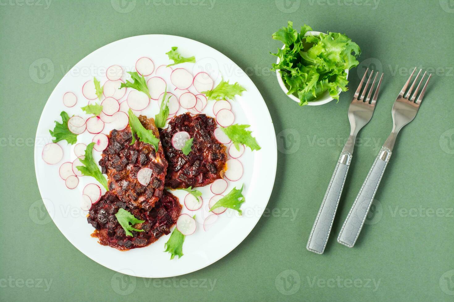 vegetal dieta Comida. beterraba bife, rabanete e friso salada folhas em uma prato e garfos em uma verde fundo foto