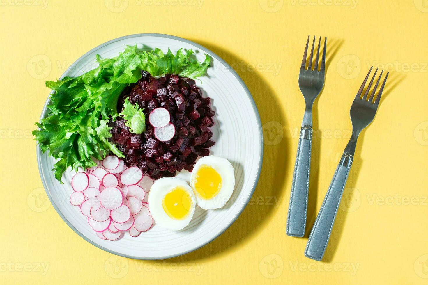 uma dietético prato fez a partir de legumes. beterraba tártaro, rabanete, friso salada e fervido ovo em uma prato e uma garfo em uma amarelo fundo. Difícil claro. diretamente acima foto