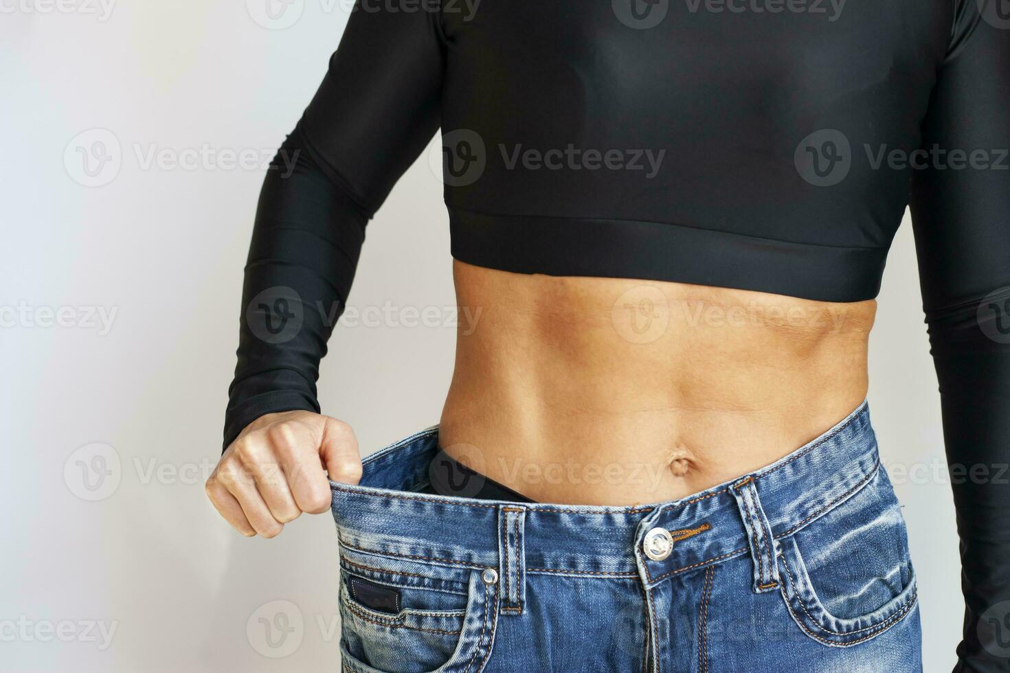 forma delgado, fino cintura, atraente fino ásia jovem mulher, mão mostrar forma dela peso perda, vestindo dentro grande, ampla ou grande demais jeans, excesso perder de dieta e exercício. pessoas corpo em forma saudável foto