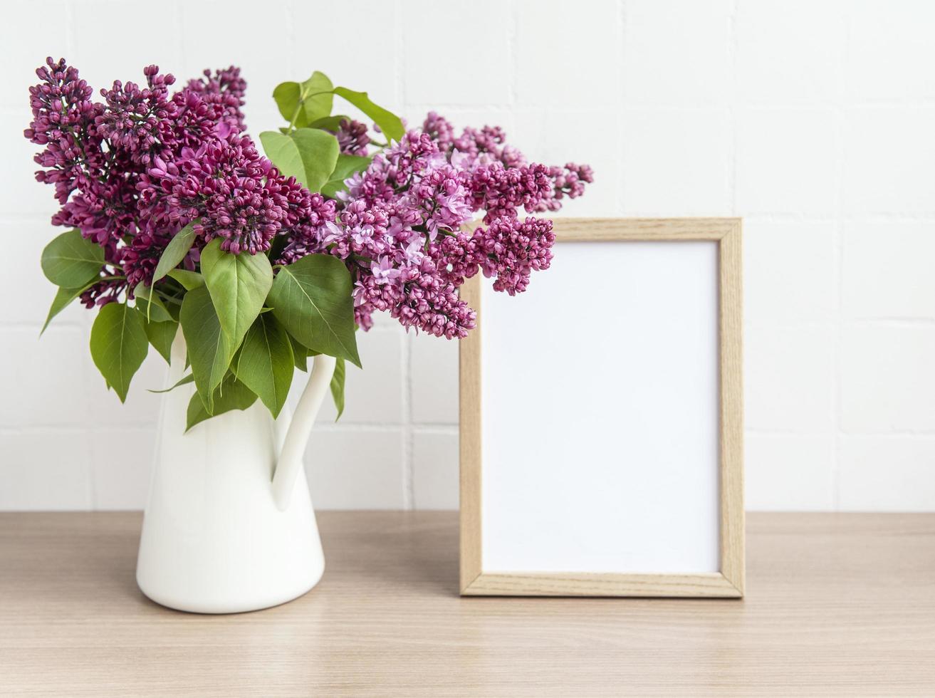 buquê de flores lilás em um vaso e moldura de madeira vazia foto