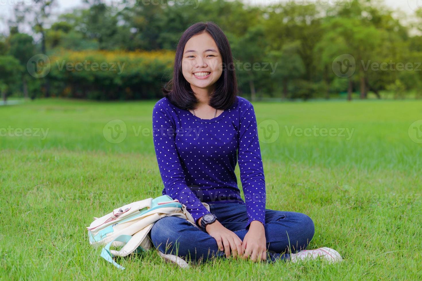 aluna asiática sentada e sorrindo no parque em um dia ensolarado de verão foto