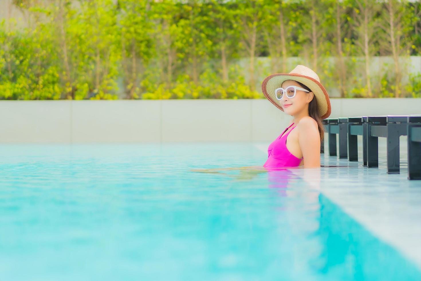 retrato bela jovem asiática relaxando sorriso ao redor de uma piscina externa em hotel resort foto