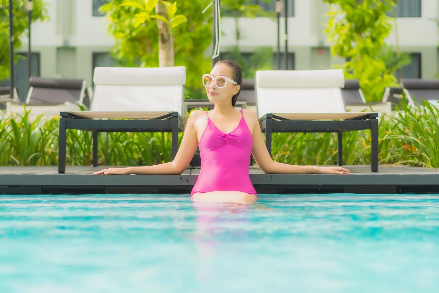 retrato bela jovem asiática relaxando sorriso ao redor de uma piscina externa em hotel resort foto