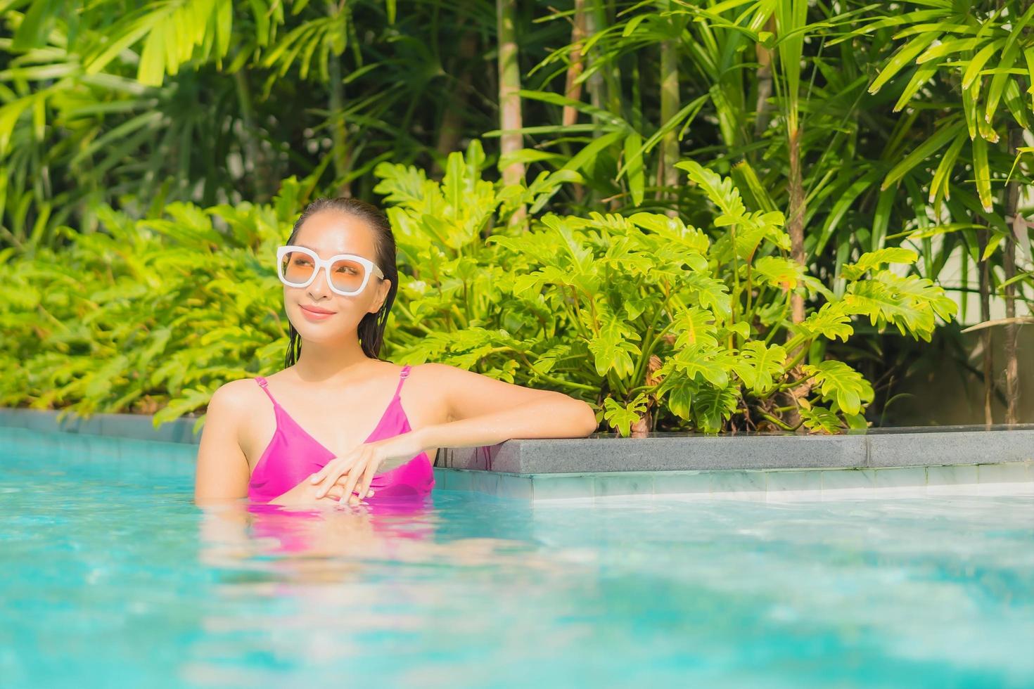 retrato bela jovem asiática relaxando sorriso ao redor de uma piscina externa em hotel resort foto