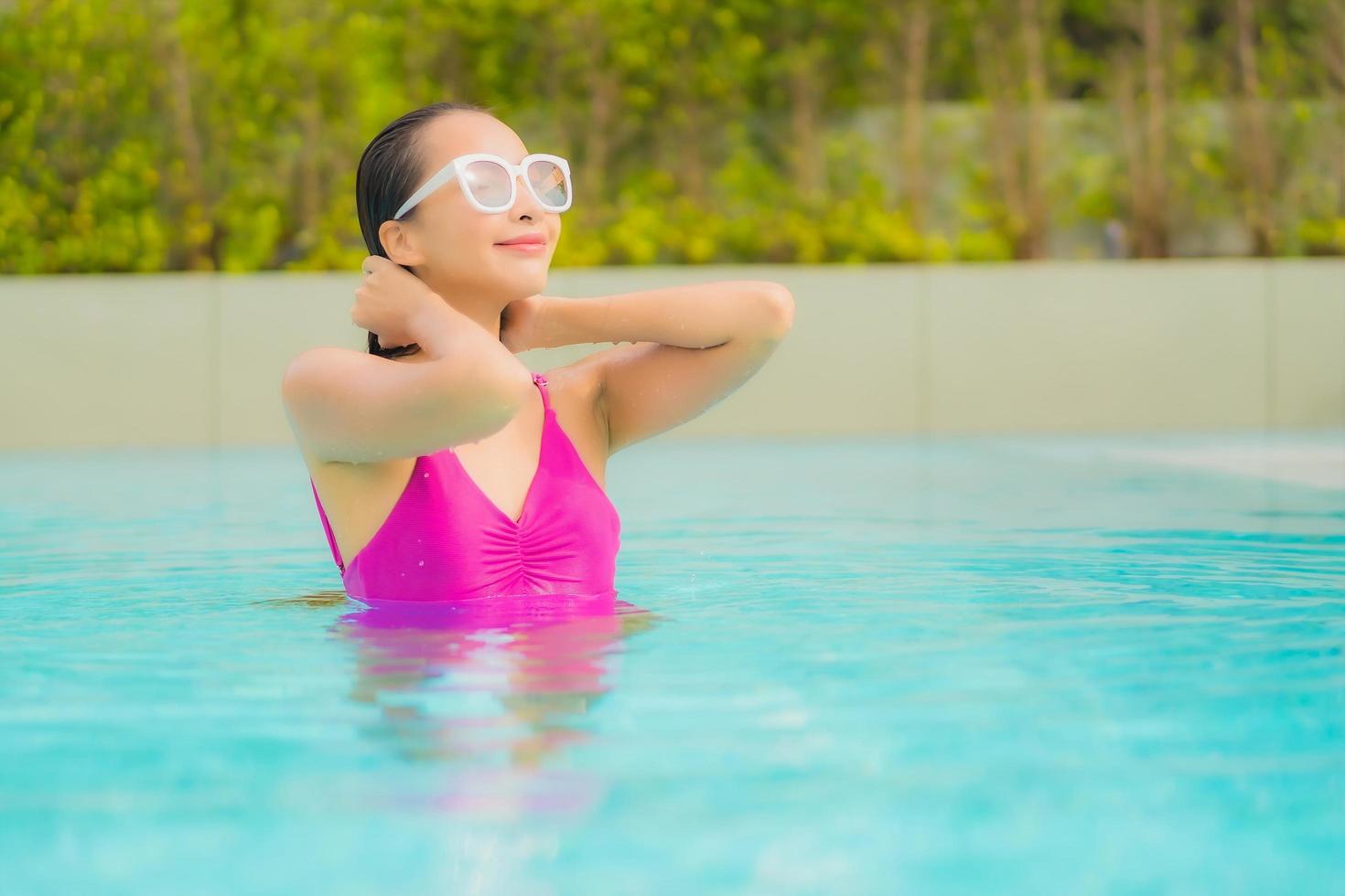 retrato bela jovem asiática relaxando sorriso ao redor de uma piscina externa em hotel resort foto