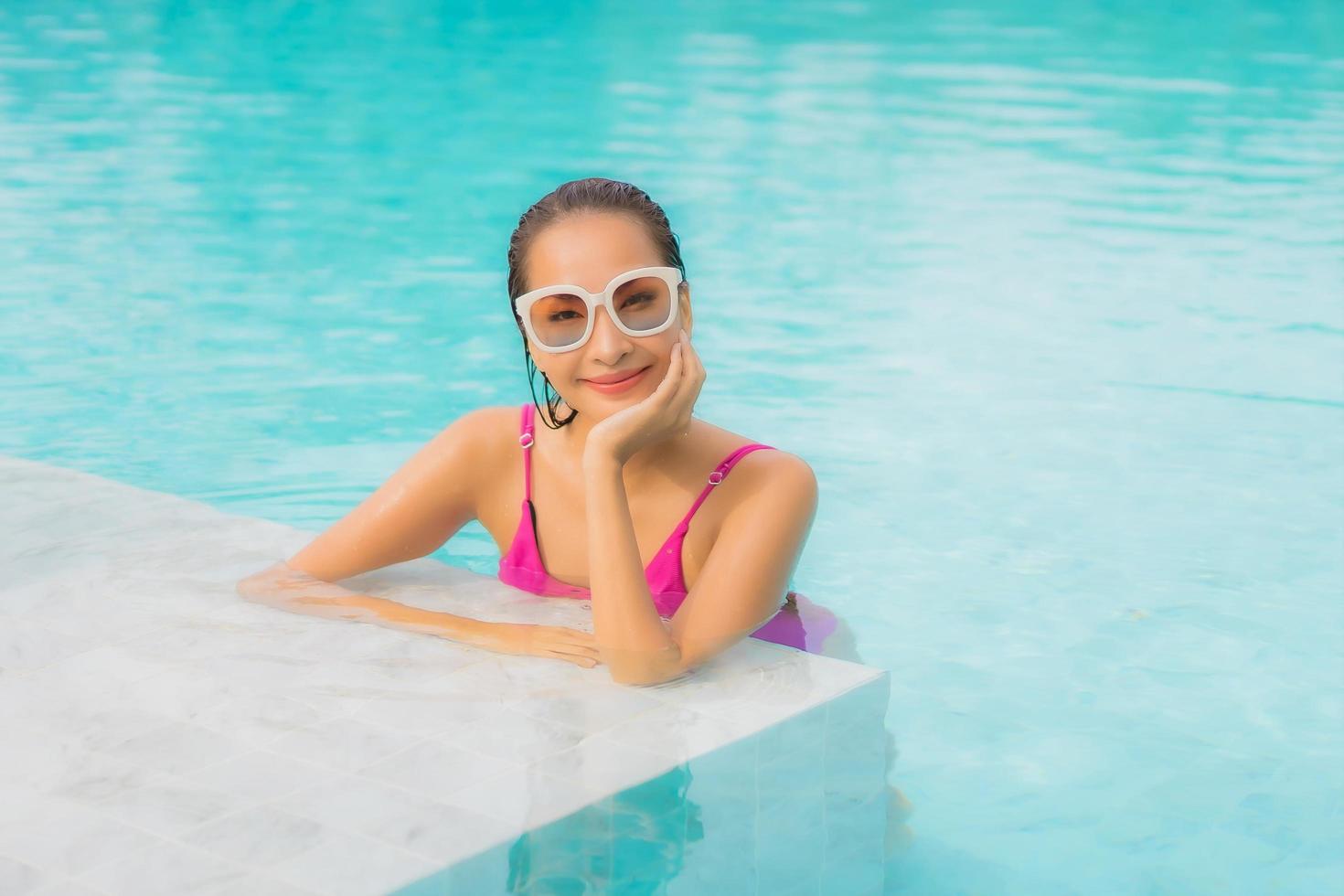 retrato bela jovem asiática relaxando sorriso ao redor de uma piscina externa em hotel resort foto