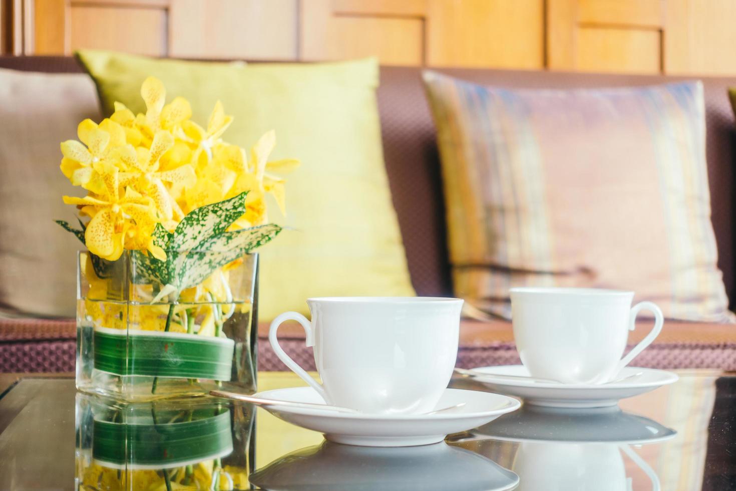 vaso de flores e xícara de café branco na mesa e travesseiro no sofá foto